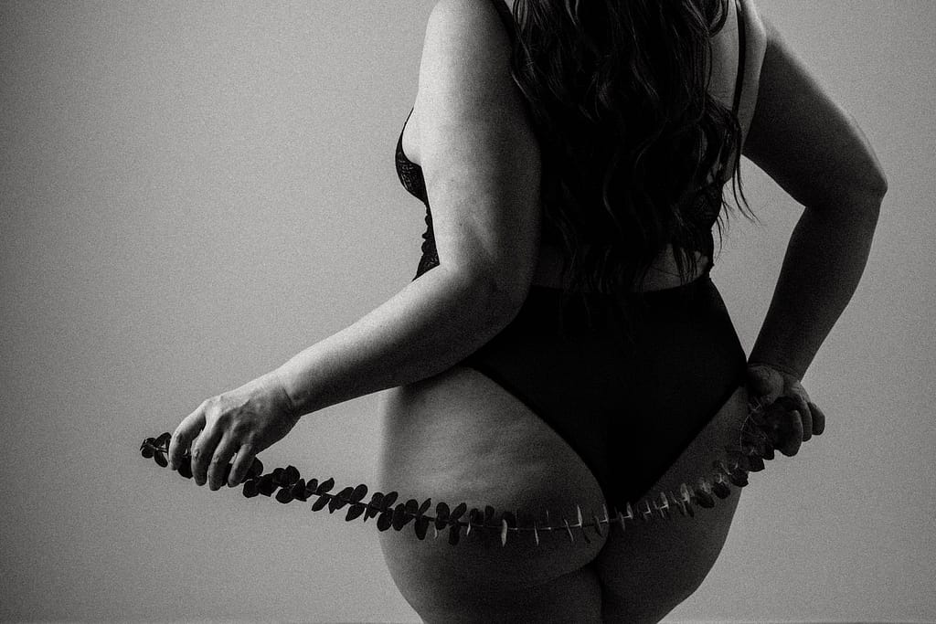 Plus size boudoir photo of the backside of a woman holding eucalyptus