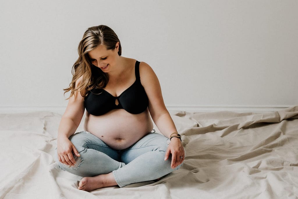maternity boudoir image of woman sitting crossed leggged wearing bra and jeans