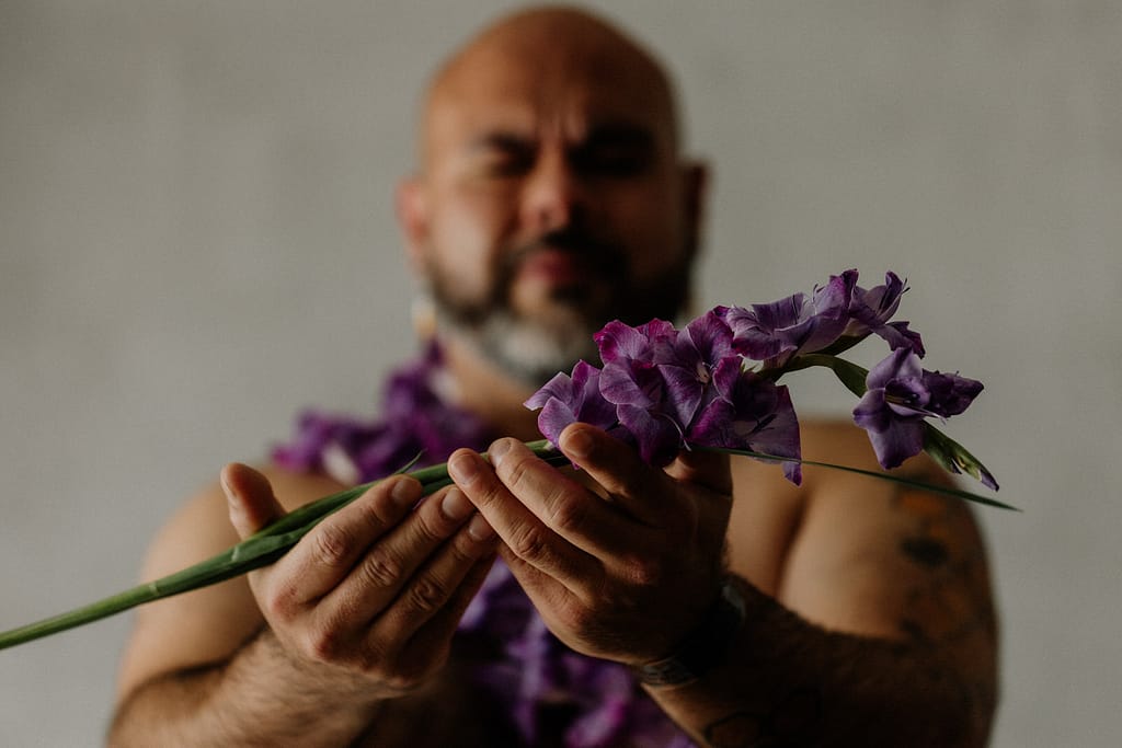 Vancouver Portrait Photographer Michele Mateus creates portraits of people with elements of nature. Pictured here is a man holding up purple flowers as an offering.