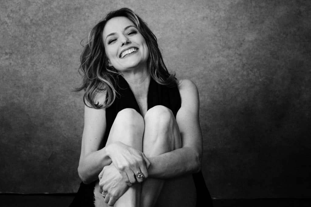 A woman sitting and hugging her knees to chest and smiling for boudoir photo