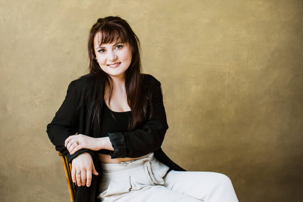 Wide shot image of a woman sitting on a chair with arm leaning on back of chair