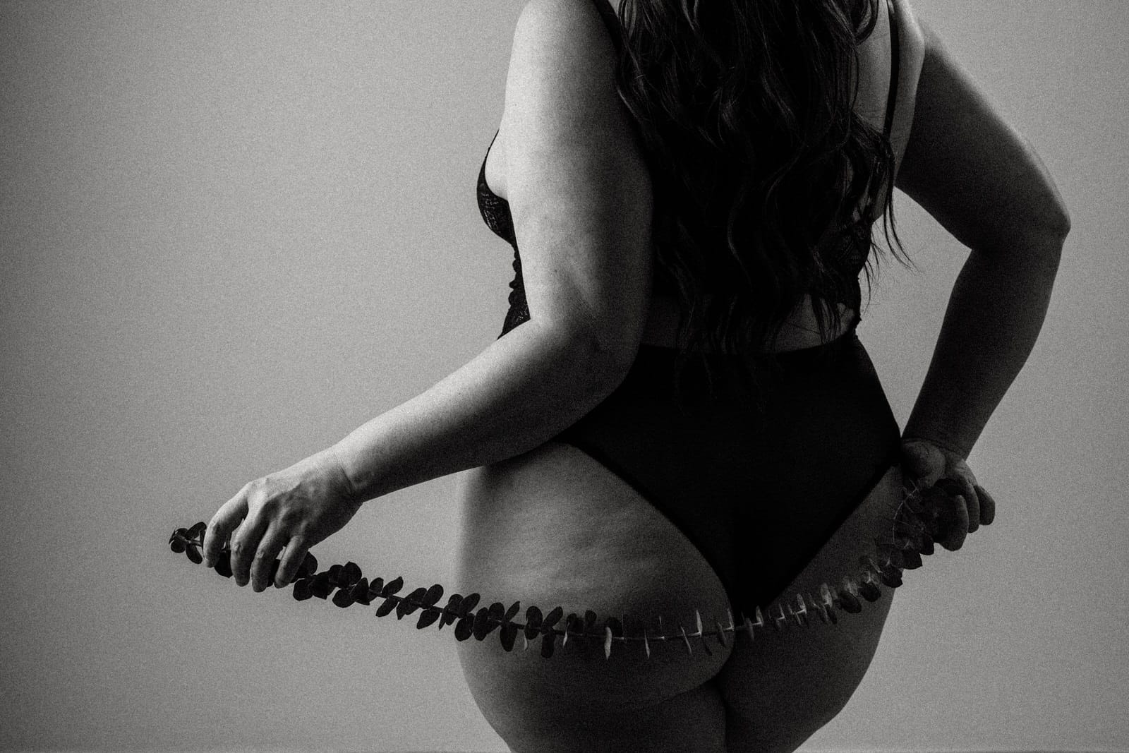 Plus size boudoir photo of the backside of a woman holding eucalyptus