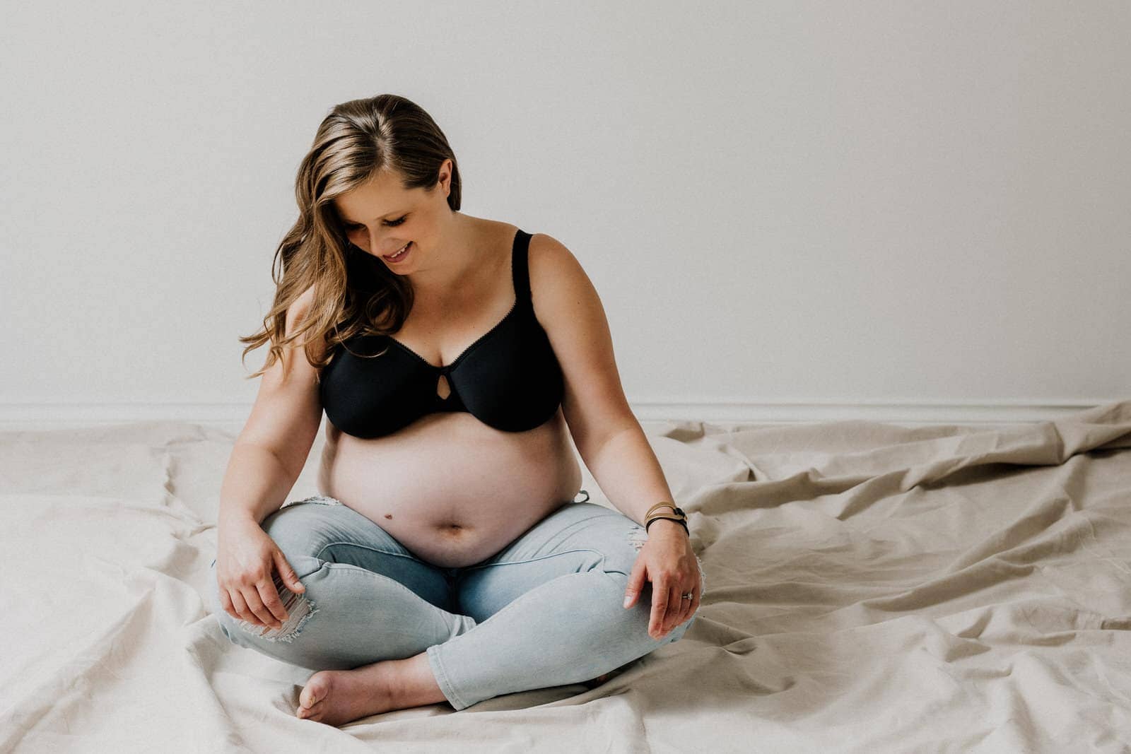 maternity boudoir image of woman sitting crossed leggged wearing bra and jeans