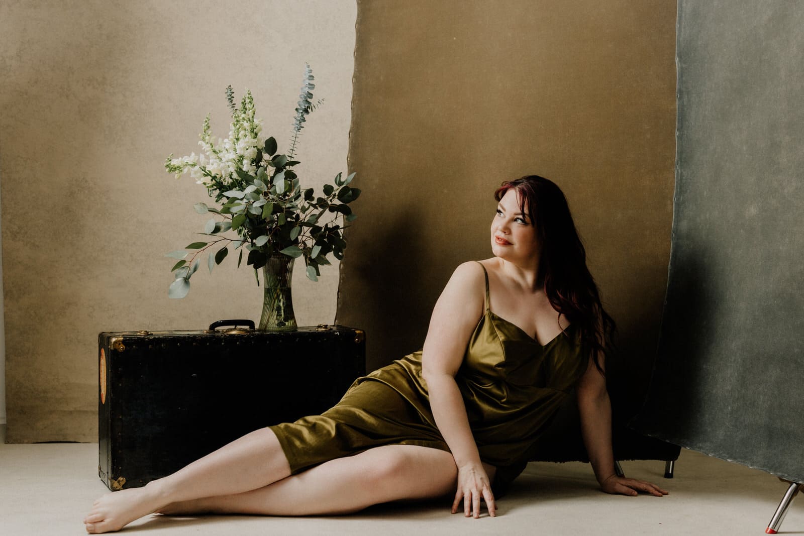 Plus size boudoir photo of a woman sitting on the floor and a vase of flowers