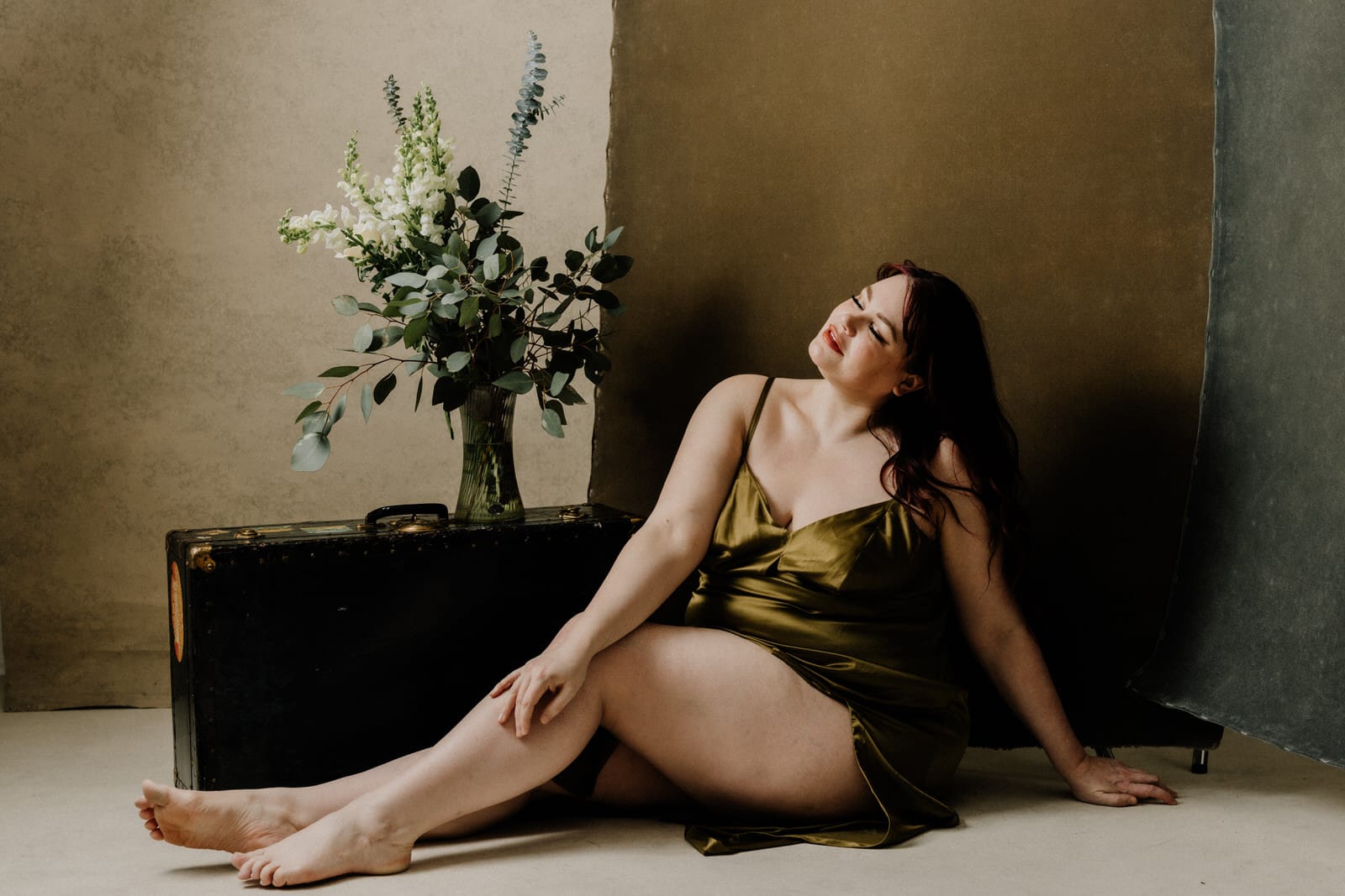 Plus size boudoir photo of a woman sitting on the floor and a vase of flowers