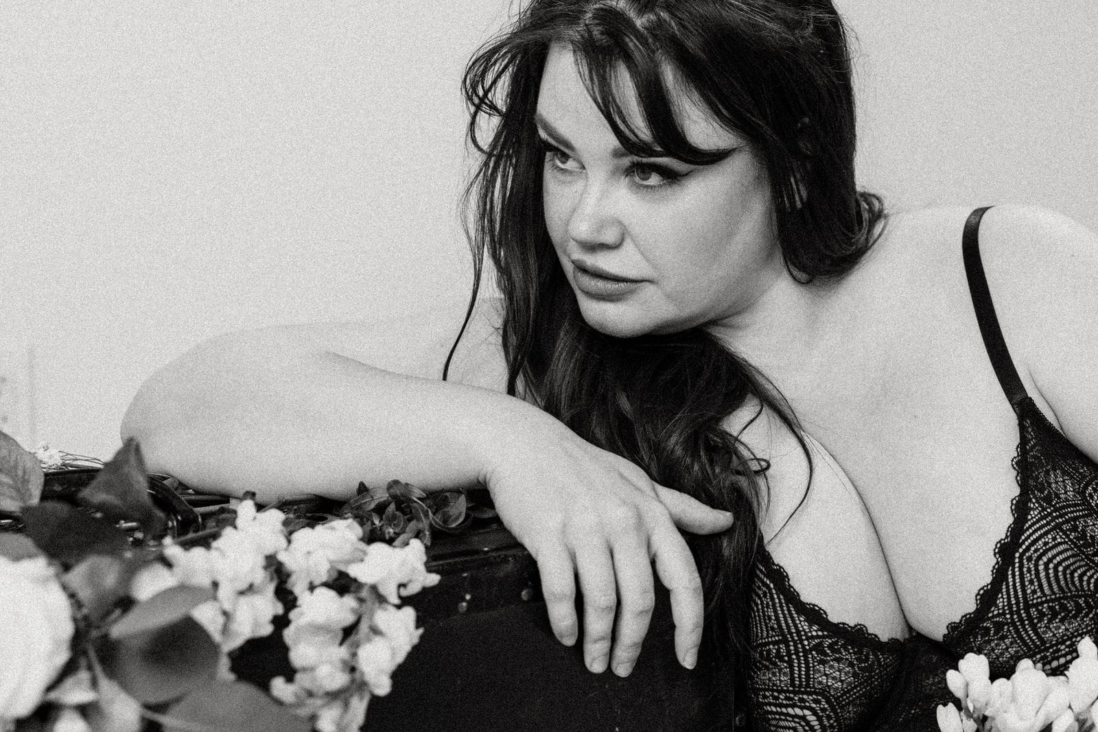 Plus size boudoir photo of a woman leaning and flowers under her arm
