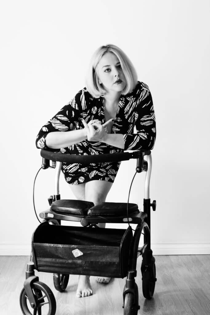 Woman with MS standing over a walker giving the f-you sign with her hands