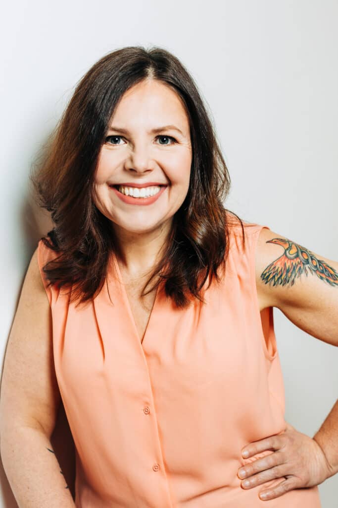 Headshots image of a woman in a v neck sleeveless top with one hand on hip