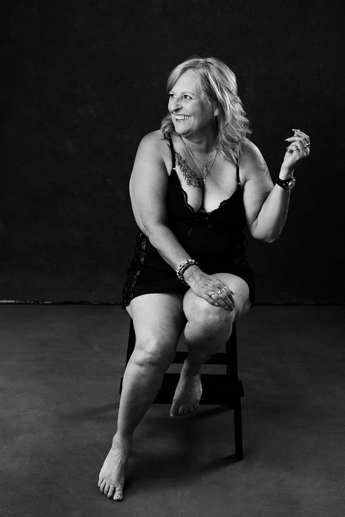 Black and white boudoir portrait of plus size women sitting on chair smiling, vancouver boudoir