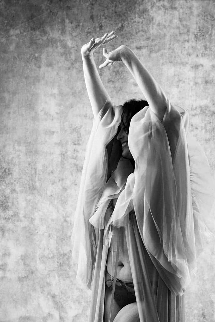 boudoir image of woman draped in tulle and hands raised in the air