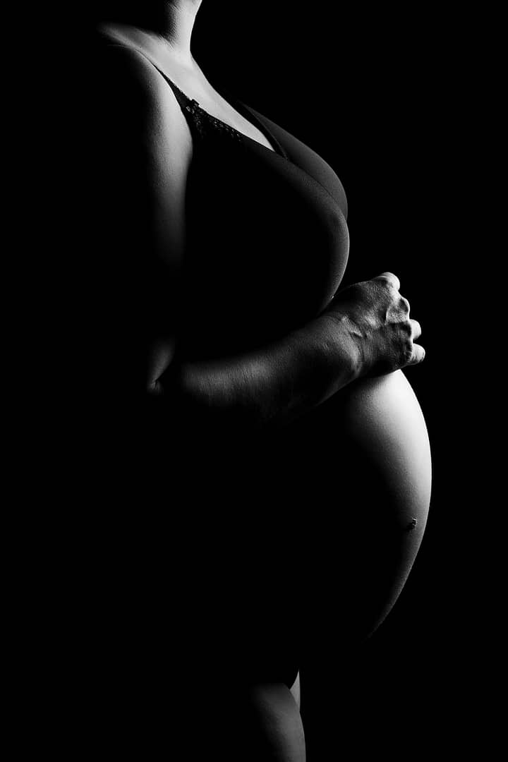 black and white boudoir maternity photographer portrait of woman wearing a bra showing her bump