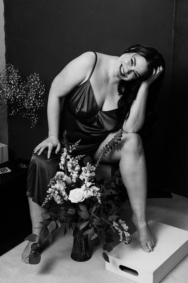 empowerment photography image of a woman sitting on a bench smiling with hand on her head and the other on her knee wearing lingerie and holding flowers