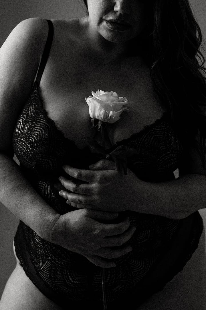 Plus size boudoir photo of a woman's midsection holding a rose to her chest