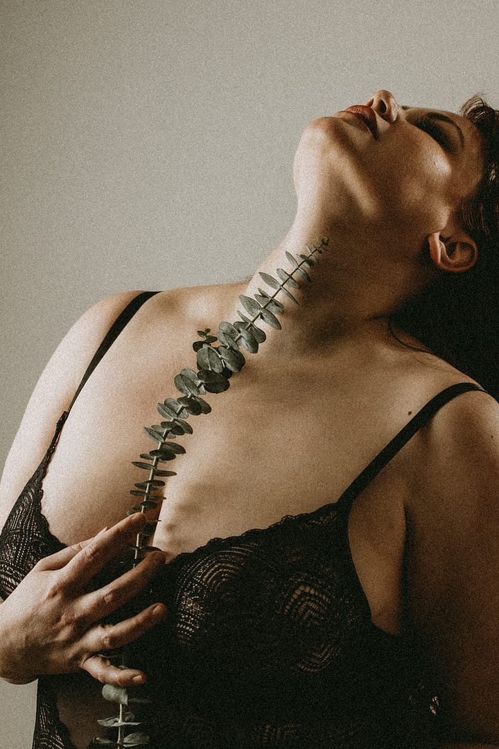 Plus size boudoir photo of a woman holding eucalyptus branch up her middle
