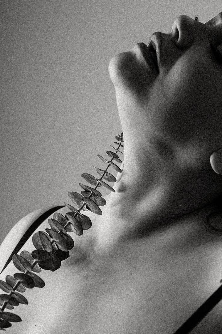close up Plus size boudoir photo of a woman's neck holding eucalyptus branch to her neck