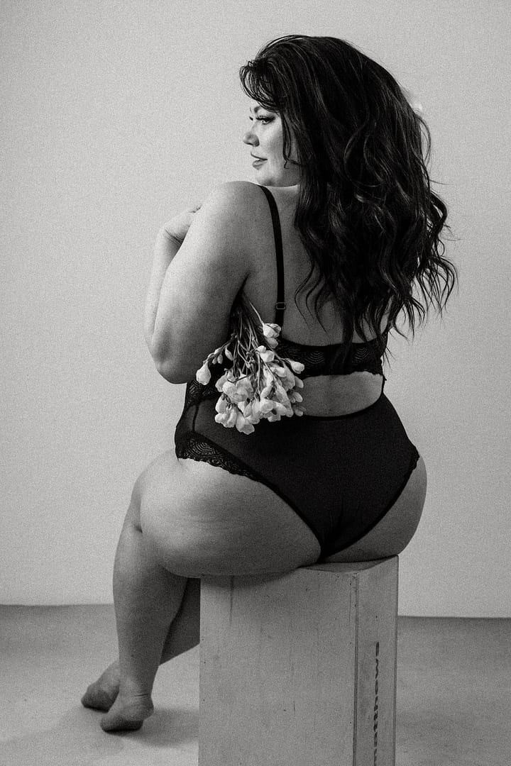 Plus size boudoir photo of a woman's back holding flowers under her arm