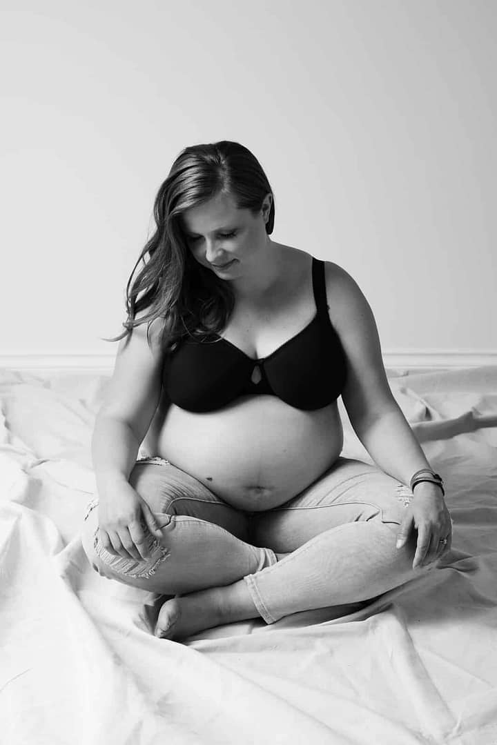 black and white image of pregnant woman sitting crossed legged wearing bra and jeans