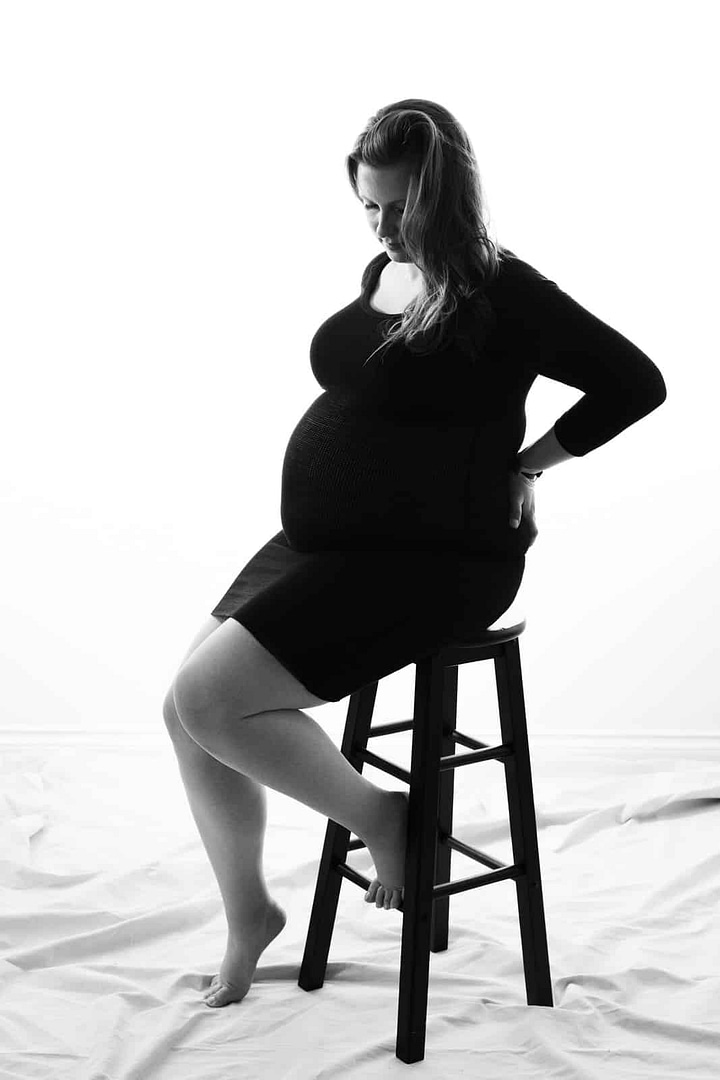 pregnant woman sitting on stool wearing dress by vancouver maternity photographer