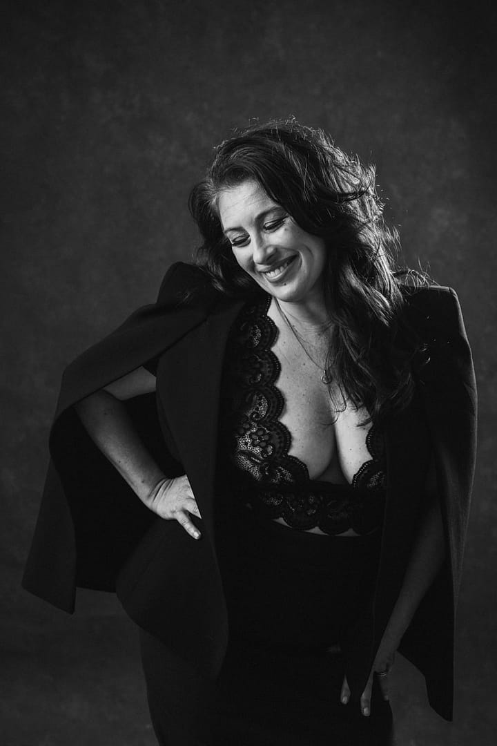 woman with hand on hip smiling, wearing low cut lace top revealing cleavage in boudoir image