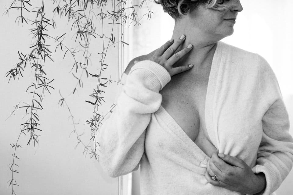 black and white boudoir photoshoot image of woman wearing a sweater pulled down revealing shoulder and cleavage and hand at her neck