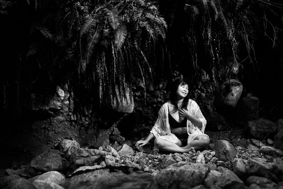woman sitting crossed legged on rocks in the forest wearing a bikini and lace robe for boudoir images