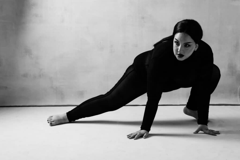 feminine embodiment boudoir photo of woman in black bodysuit stretching in a lunge