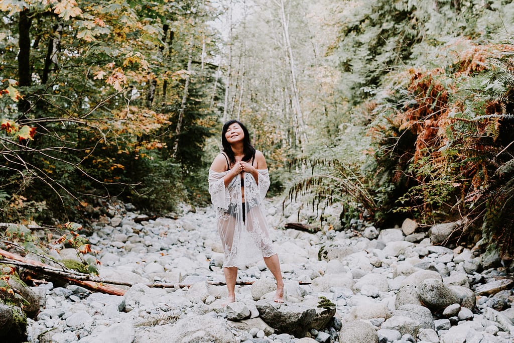 Invest in you with an outdoor boudoir photo shoot like this woman in a white lace robe standing in a dry creek bed