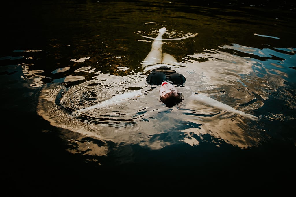 Woman with red lips and wearing a black swimsuit floating on her back in a body of water