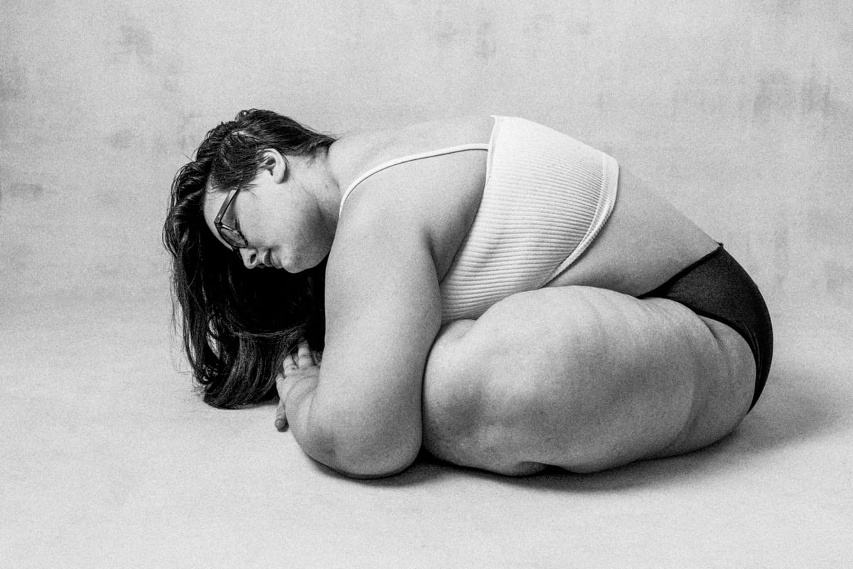 feminine embodiment boudoir image of woman wearing panties and bra sitting crossed legged leaning over touching the floor