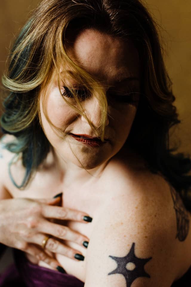 Colour boudoir image of a woman with closed eyes and bare shoulders and her hand at her chest