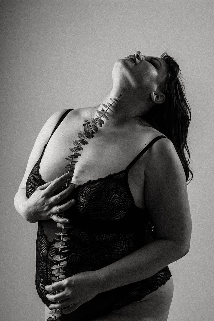 Plus size boudoir photo of a woman holding eucalyptus branch up her middle, empowering portraits