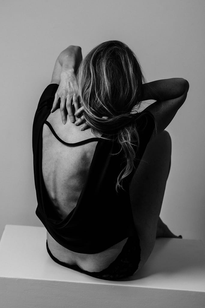 vancouver classy boudoir image of woman sitting with hands at back of neck revealing her back in a backless top