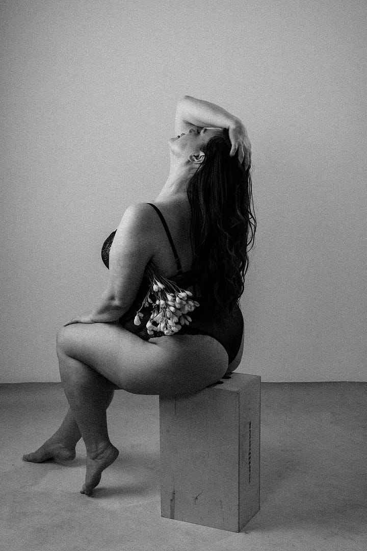 Plus size boudoir photo of a woman sitting holding flowers across her legs