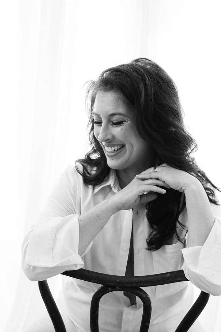 white shirt boudoir image of woman smiling with hands clasped under chin