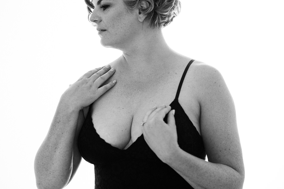 Woman wearing black bodysuit in boudoir photoshoot vancouver with one hand at chest and the other at shoulder