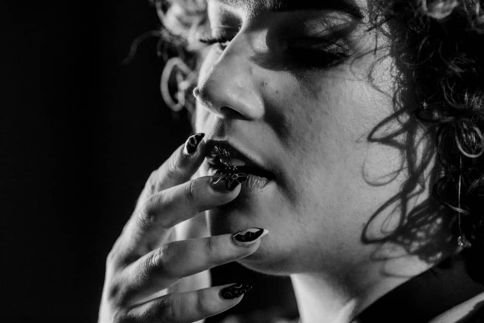 woman with curly hair holding fingers and long finger nails up to her lips in boudoir image