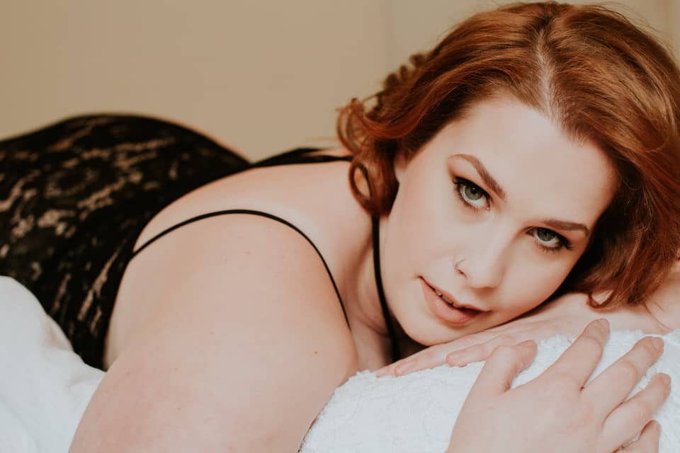 plus size boudoir photo of red head woman laying on pillow wearing lingerie
