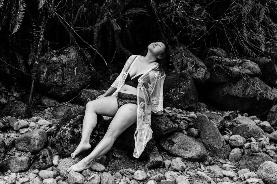 Woman in a bikini and lace robe sitting on a rock in a riverbed